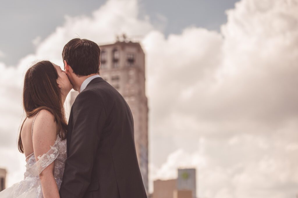 An image of a bride kissing the cheeks of the groom on a rooftop on their wedding day