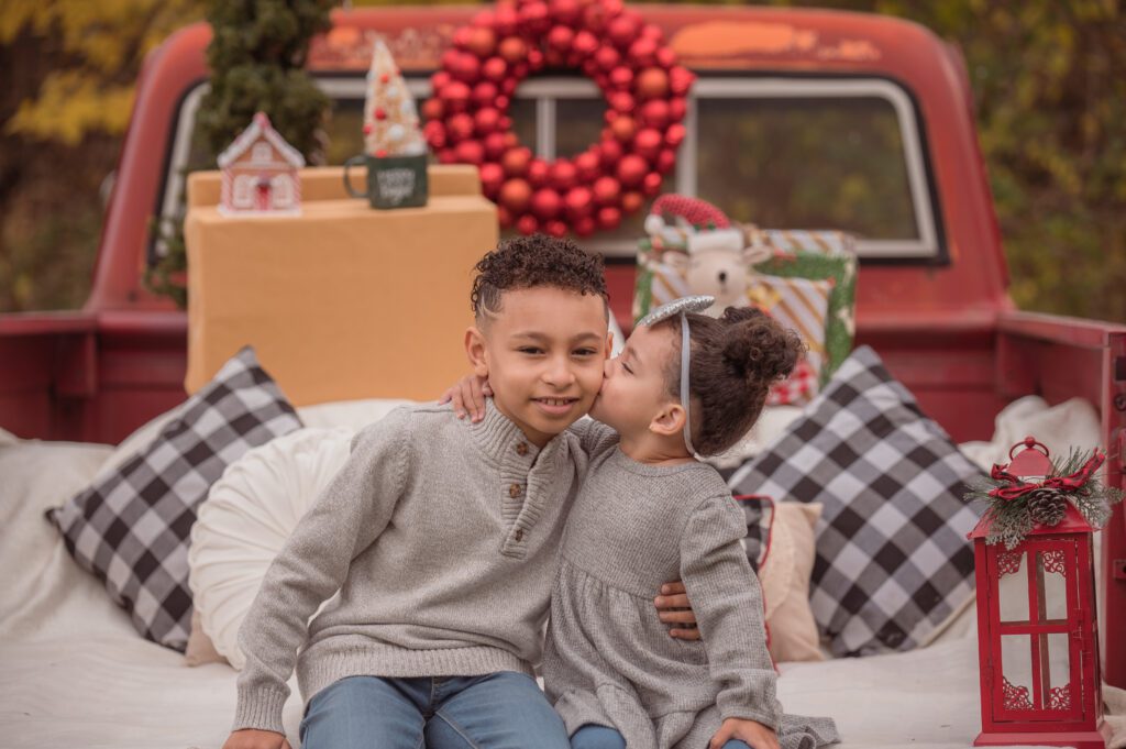 Kid sister kissing his elder brother, on a Red Truck for their Holiday family picture. 